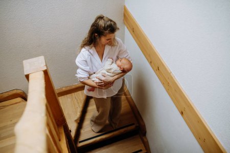 Photo for Top view of mother carrying little baby in arms down the stairs. Looking at newborn children and smiling. - Royalty Free Image