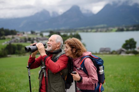 Téléchargez les photos : Couple âgé actif randonnée ensemble dans les montagnes d'automne. Les touristes seniors profitant de la nature regardent à travers des jumelles. - en image libre de droit