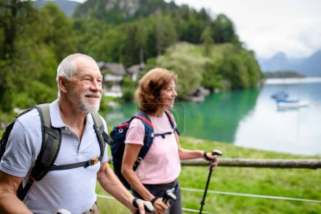 Foto de Retrato de pareja de ancianos activos caminando juntos en las montañas. Turistas mayores caminando con bastones de trekking para estabilidad. - Imagen libre de derechos
