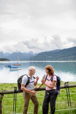 Téléchargez les photos : Couple âgé actif marchant ensemble dans une montagne. Boire du café et avoir une collation saine, pour obtenir de l'énergie. Touriste sénior avec sacs à dos se reposant pendant la randonnée. - en image libre de droit