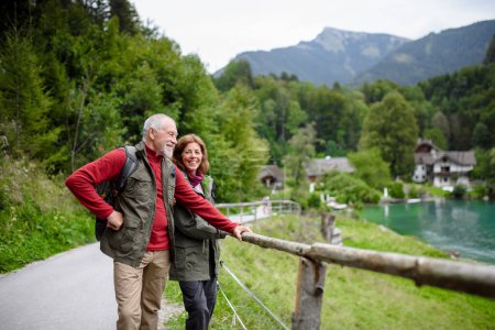 Foto de Pareja de ancianos activos caminando juntos en las montañas de otoño. Turistas mayores disfrutando de vista al lago. - Imagen libre de derechos