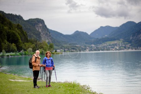 Téléchargez les photos : Portrait d'un beau couple de personnes âgées actives marchant ensemble dans les montagnes printanières. Touristes seniors s'embrassant devant un lac. - en image libre de droit