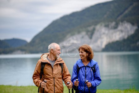 Foto de Retrato de una hermosa pareja activa de ancianos que caminan juntos en las montañas de primavera. Turistas mayores de pie frente a un lago. - Imagen libre de derechos