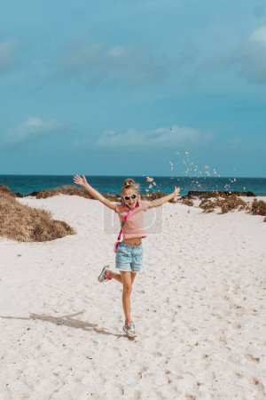 Foto de Chica lanzando saltos de arena, de pie en la playa. Vacaciones familiares de verano junto al mar. - Imagen libre de derechos