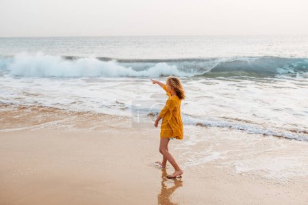 Photo for Young girl on the beach. Rear view of blonde girl enjoying sandy beach, looking at crystalline sea in Canary Islands. Concept of beach summer vacation with kids. - Royalty Free Image