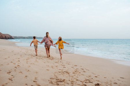 Téléchargez les photos : Mère avec deux enfants sur la plage. Jeune famille profitant de la plage de sable dans les îles Canaries. Concept de vacances d'été à la plage avec les enfants. - en image libre de droit