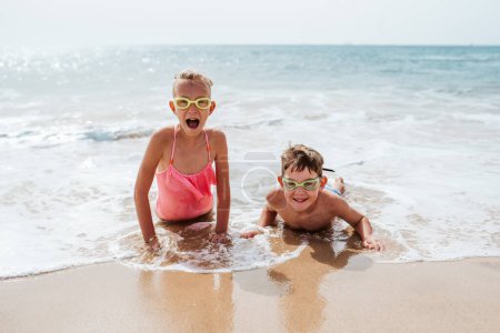 Photo for Siblings playing on beach, running, having fun. Smilling girl and boy on sandy beach with vulcanic rocks of Canary islands. Concept of a family beach summer vacation with kids. - Royalty Free Image