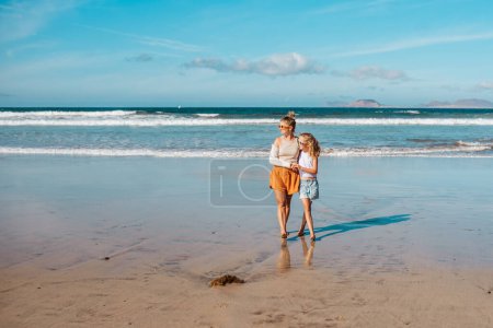 Photo for Daughter with mother with broken arm on beach. Arm cast, injured during family vacation in holiday resort. Concept of family beach summer vacation with injury. - Royalty Free Image