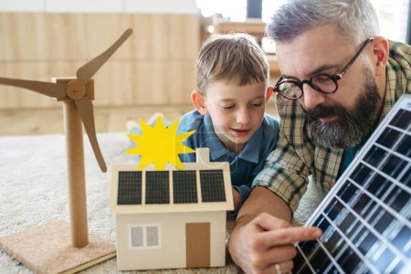 Père expliquant les énergies renouvelables, l'énergie solaire et l'enseignement sur le mode de vie durable son jeune fils. Jouer avec le modèle de maison avec des panneaux solaires. Apprendre par le jeu.