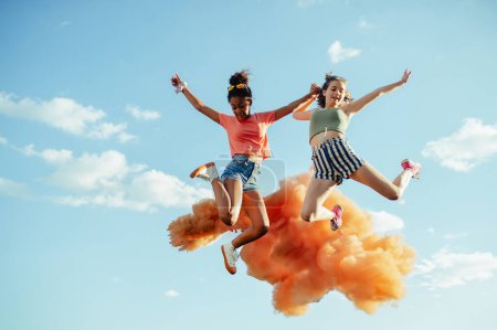 Foto de Vista de ángulo bajo de jóvenes amigas adolescentes saltando alto. Divertirse al aire libre en la ciudad, de pie en la pared de hormigón. - Imagen libre de derechos