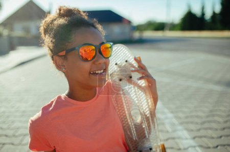 Téléchargez les photos : Jeune adolescente avec des planches à roulettes passer du temps en ville pendant la chaude journée de vacances d'été. Assis sur le parking. - en image libre de droit