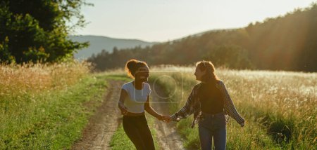 Photo for Cheerful young teenager girl best friends spending time in nature, during sunset. Girls on walk by forest, summer holidays. Banner with copyspace. - Royalty Free Image