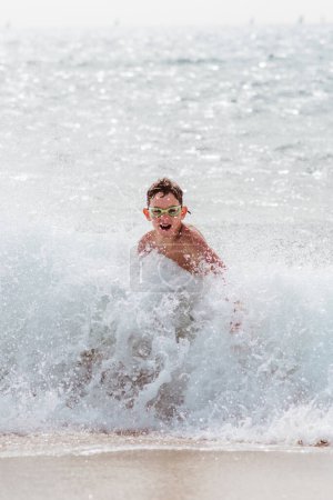 Photo for Young boy playing, running and splashing in strong sea waves. Smilling boy in swimsuit looking at waves. Concept of a beach summer vacation with kids. - Royalty Free Image