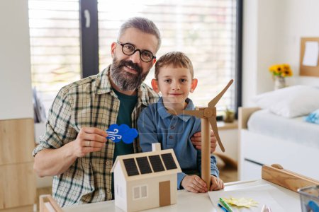 Vater erklärt erneuerbare grüne Energien, unterrichtet seinen kleinen Sohn über nachhaltigen Lebensstil. Das Spiel mit dem Modell eines Hauses mit Sonnenkollektoren, Windturbinen zu Hause. Lernen durch Spielen.