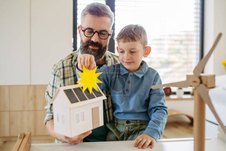 Vater erklärt erneuerbare grüne Energien, unterrichtet seinen kleinen Sohn über nachhaltigen Lebensstil. Das Spiel mit dem Modell eines Hauses mit Sonnenkollektoren, Windturbinen zu Hause. Lernen durch Spielen.