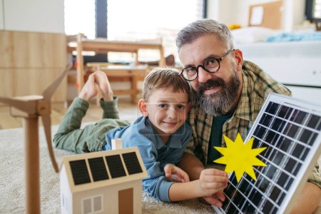 Vater erklärt seinem kleinen Sohn erneuerbare Energien, Solarenergie und lehrt über nachhaltigen Lebensstil. Spiel mit dem Modell eines Hauses mit Sonnenkollektoren. Lernen durch Spielen.