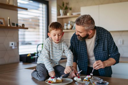 Photo for Boy filling pancake with fruit, sweets. Father spending time with son at home, making snack together, cooking. Weekend activities for single dad with young boy. Fathers day concept. - Royalty Free Image
