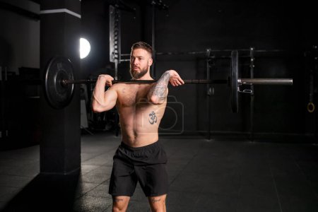 Photo for Strong man performing front squat, barbell resting on front shoulders, bare chest. Routine workout for physical and mental health. - Royalty Free Image