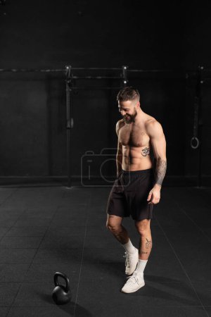 Photo for Man lifting dumbbell from gym floor, wearing only shorts, bare chest. Routine workout for physical and mental health. - Royalty Free Image