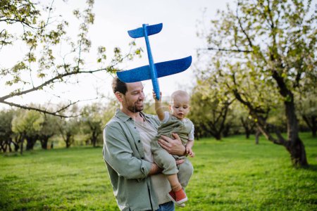 Photo for Father and toddler playing with foam glider plane. A Single dad having fun with baby during warm spring day. Fathers day concept. - Royalty Free Image