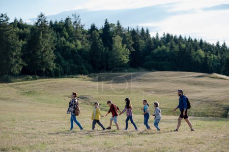 Foto de Jóvenes estudiantes caminando por el prado durante la clase de biología, tomados de la mano. Profesores dedicados durante la enseñanza activa al aire libre sobre ecosistema y naturaleza. - Imagen libre de derechos