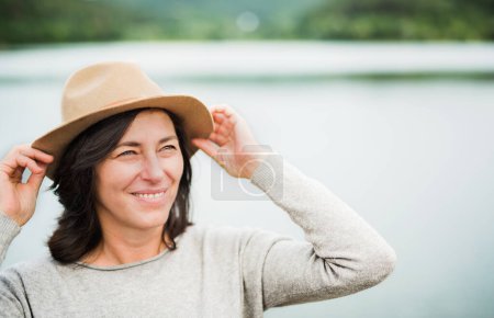 Foto de Retrato de hermosa mujer madura con sombrero, de pie junto al lago, estanque. - Imagen libre de derechos
