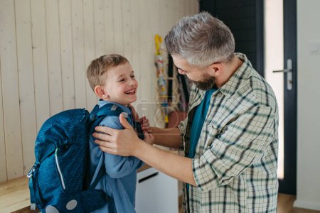 Vater hilft Sohn, sich auf Kindergarten, Vorschule vorzubereiten. Rucksack auf den Rücken gelegt.