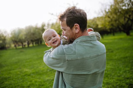 Téléchargez les photos : Un père tenant un petit bébé, jouant, s'amusant pendant la chaude journée de printemps. Concept de fête des pères. - en image libre de droit