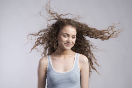 Photo for Portrait of a gorgeous teenage girl with curly hair, blowing in wind. Studio shot, white background with copy space. - Royalty Free Image