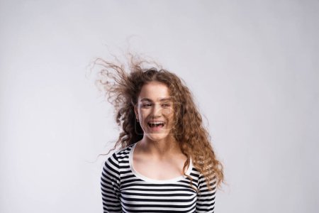 Téléchargez les photos : Portrait d'une magnifique adolescente aux cheveux bouclés, soufflant dans le vent. Plan studio, fond blanc avec espace de copie. - en image libre de droit