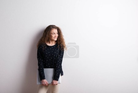 Foto de Retrato de una hermosa adolescente con el pelo rizado, sosteniendo el cuaderno, apoyado contra la pared. Captura de estudio, fondo blanco con espacio de copia. - Imagen libre de derechos