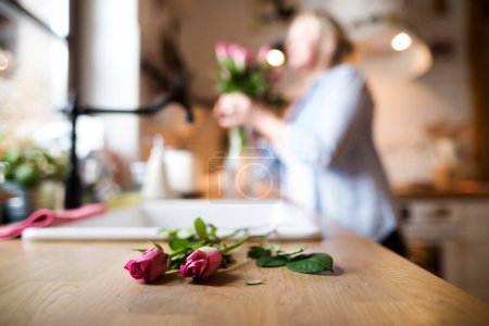 Téléchargez les photos : Belle femme mûre arrangeant un bouquet de roses dans un vase, un passe-temps et de détente. Femme âgée vivant seule, profitant d'une journée paisible week-end. - en image libre de droit