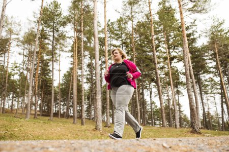 An overweight woman running in nature. Exercising outdoors for people with obesity.