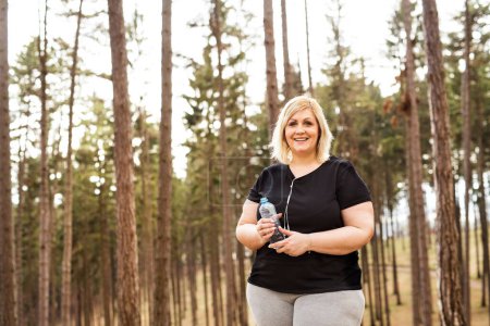 An overweight woman preparing for run in nature. Exercising outdoors for people with obesity.