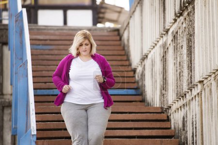 Femme en surpoids courant en ville, en bas des escaliers. Exercice en plein air pour les personnes obèses.
