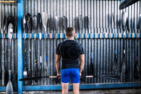 Photo for Rear view of young canoeist standing in front of wall with paddles. Concept of canoeing as dynamic, adventurous sport - Royalty Free Image
