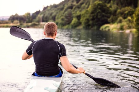 Kanufahrer sitzt im Kanu mit Paddel im Wasser. Konzept des Kanufahrens als dynamischer und abenteuerlicher Sport. Rückansicht, Sportler blickt auf Wasseroberfläche, paddelt.