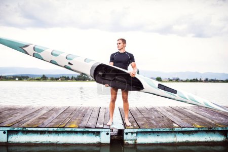 Jeune canoéiste tenant canot et pagaie, allant dans l'eau, debout sur un quai en bois. Concept du canoë-kayak comme sport dynamique et aventureux.