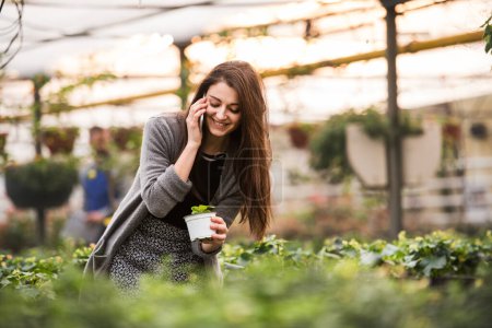 Photo for Beautiful business owner phone calling with customer, ordering flowers and seedlings. Small greenhouse business. Offering wide range of plants during spring gardening season. - Royalty Free Image
