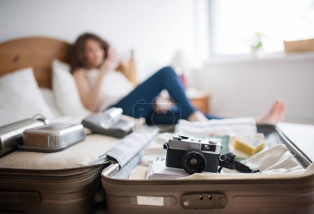 Téléchargez les photos : Belle femme couchée sur le lit à côté de valise.. Voyageur féminin solo se préparant pour le voyage. - en image libre de droit