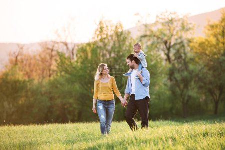 Vater trägt Kleinkind auf Schultern. Familie im Freien beim Spaziergang in der frühlingshaften Natur. Glücklicher Moment in der Familie.