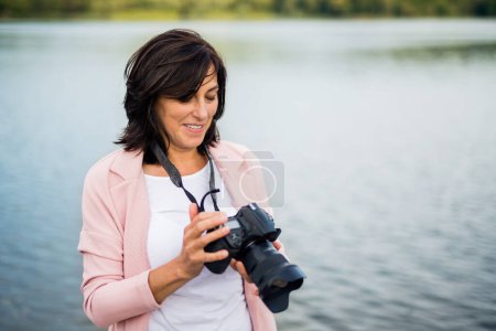Photo for Portrait of beautiful mature woman on vacation. Taking photos with professional camera, capturing beauty in nature around her. - Royalty Free Image
