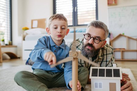 Téléchargez les photos : Père expliquant les énergies vertes renouvelables, enseignant le mode de vie durable à son jeune fils. Jouer avec le modèle de maison avec des panneaux solaires, éolienne à la maison. Apprendre par le jeu. - en image libre de droit