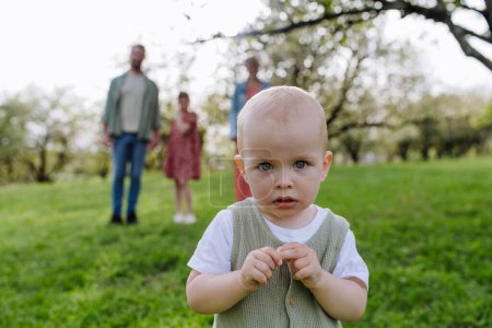 Foto de Retrato de lindo bebé niño de pie frente a su familia, caminando al aire libre en la naturaleza de primavera.Familia nuclear. - Imagen libre de derechos