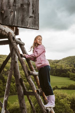 Girl on ladder of hunting blind during their walk in forest, climbing up to observe beautiful spring nature, wildlife. Viewing tower.