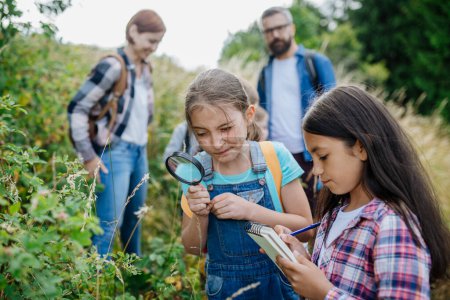 Junge Schüler lernen im Biologieunterricht etwas über die Natur, das Ökosystem Wald und beobachten Wildpflanzen mit der Lupe. Engagierte Lehrer während der aktiven Ausbildung im Freien. Lehrer