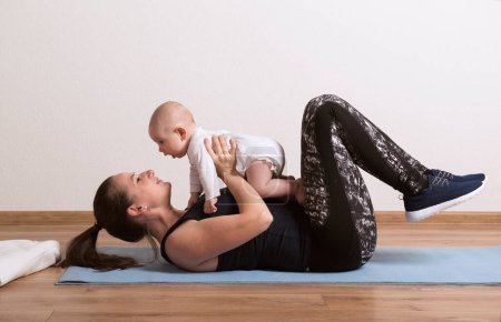 Foto de Ejercicio en casa para la madre y el bebé, mamá y yo entrenamiento. Actividad física para la madre mientras se une a los niños pequeños. - Imagen libre de derechos