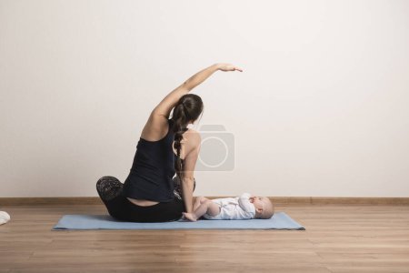 Foto de Ejercicio en casa para la madre y el bebé, mamá y yo entrenamiento. Actividad física para la madre mientras se une a los niños pequeños. - Imagen libre de derechos