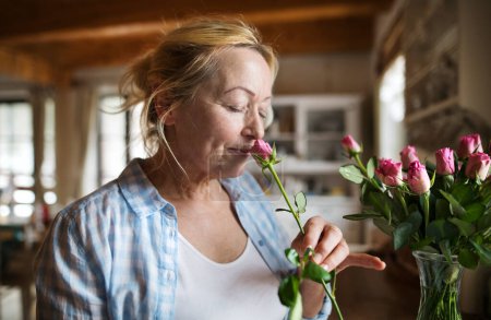 Hermosa mujer madura organizando un ramo de rosas en un jarrón, un hobby y relajación. Mujer mayor viviendo sola, disfrutando de un fin de semana tranquilo.