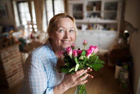 Hermosa mujer madura organizando un ramo de rosas en un jarrón, un hobby y relajación. Mujer mayor viviendo sola, disfrutando de un fin de semana tranquilo.